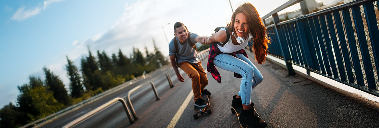 Obrázek zobrazuje muže a ženu jedoucí přes most na skateboardech