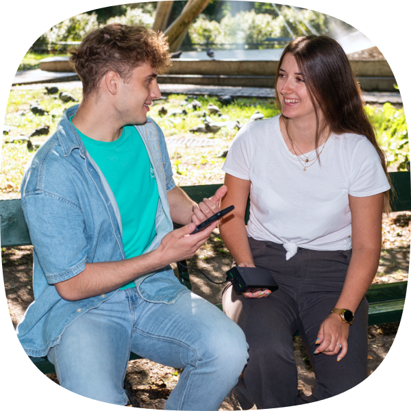 Zdjęcie przedstawia mężczyznę oraz kobietę na ławce w parku ładujących telefon za pomocą PowerPlay 30